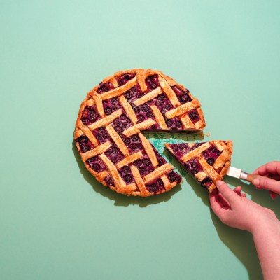 Above view with a woman's hands grabbing a slice of blueberries tart. Delicious homemade pie with a lattice crust and blueberries filling