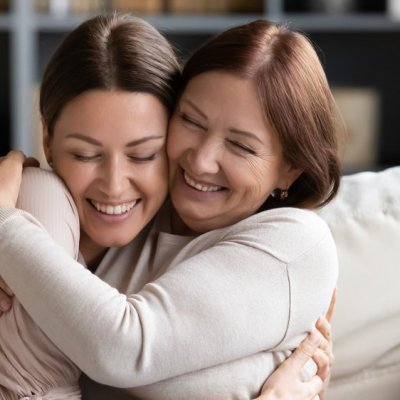 Affectionate loving middle-aged mother cuddling grownup child, amazed by good news. Excited to see daughter, happy senior older mom cuddling her, sitting together on a comfortable sofa in the living r