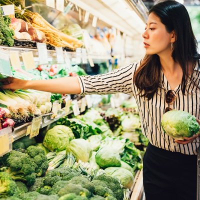 asian local woman buy vegetables and fruits in supermarket. young chinese lady holding green leaf vegetable and picking choosing green onion on cold open refrigerator. elegant female grocery shopping