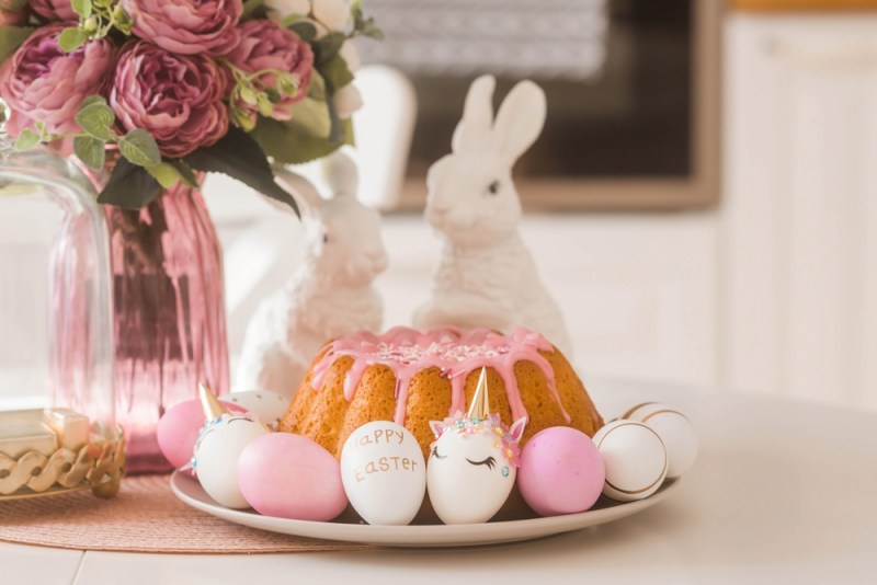 Banner. Minimal easter concept. Easter cake, rabbits and eggs in the form of a unicorn and with a gold pattern on a white table. Copy space for text. The portfolio contains more Easter pictures.