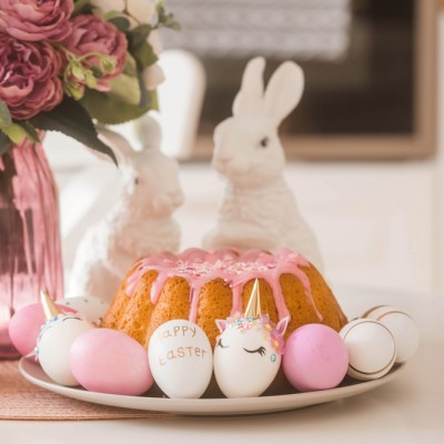 Banner. Minimal easter concept. Easter cake, rabbits and eggs in the form of a unicorn and with a gold pattern on a white table. Copy space for text. The portfolio contains more Easter pictures.