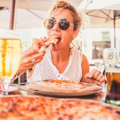 Beautiful adult caucasian woman eating italian food pizze - man couple point of view with beer and fresh drink on the table - people enjoying restaurant together sitting outdoor