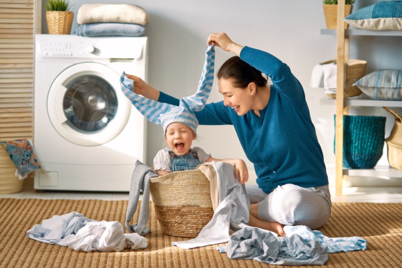 Beautiful young woman and child girl little helper are having fun and smiling while doing laundry at home.
