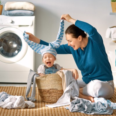 Beautiful young woman and child girl little helper are having fun and smiling while doing laundry at home.