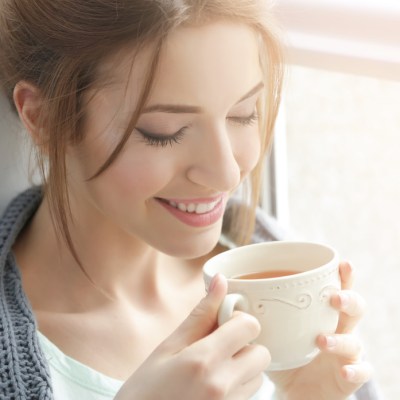 Beautiful young woman drinking tea near window at home