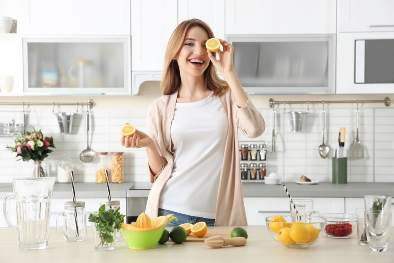 Beautiful young woman preparing lemonade in kitchen. Lemon-themed kitchen decor