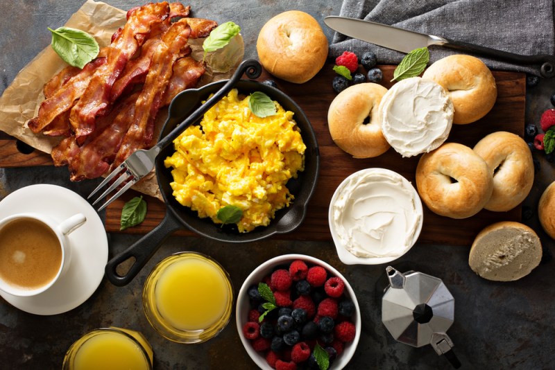 Big breakfast with bacon, bagels and scrambled eggs on the table overhead