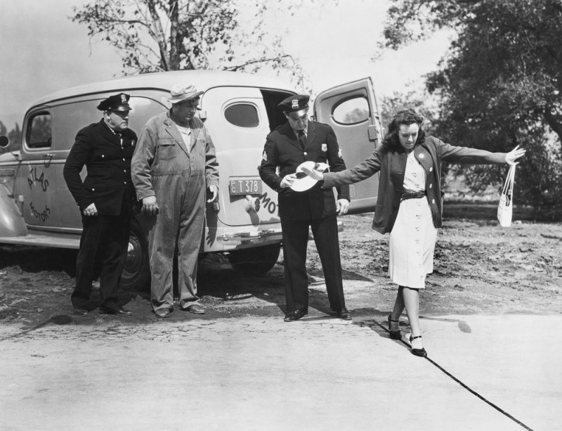 black and white photo of female walking the line in a field sobriety test as officers look on