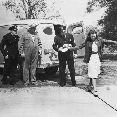 black and white photo of female walking the line in a field sobriety test as officers look on