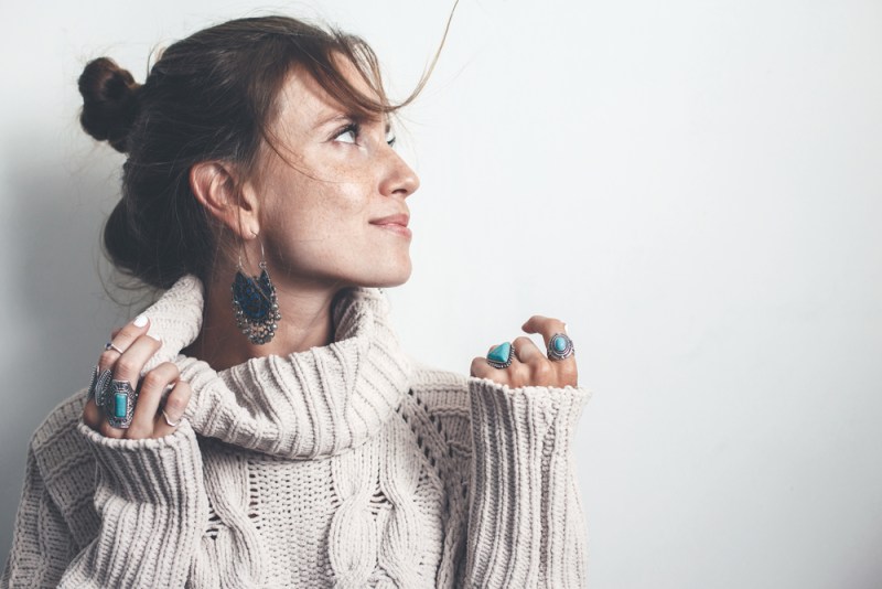 Boho jewelry on model: ethnic stone rings and earrings. Beautiful woman wearing warm woolen sweater and fashion jewellery. Minimal style and pastel tone.