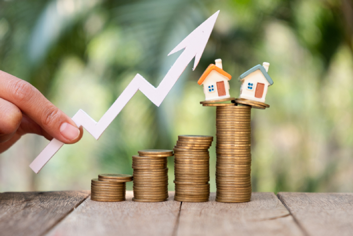Businessperson's Hand Holding Arrow Over Stacked Coins With House Models