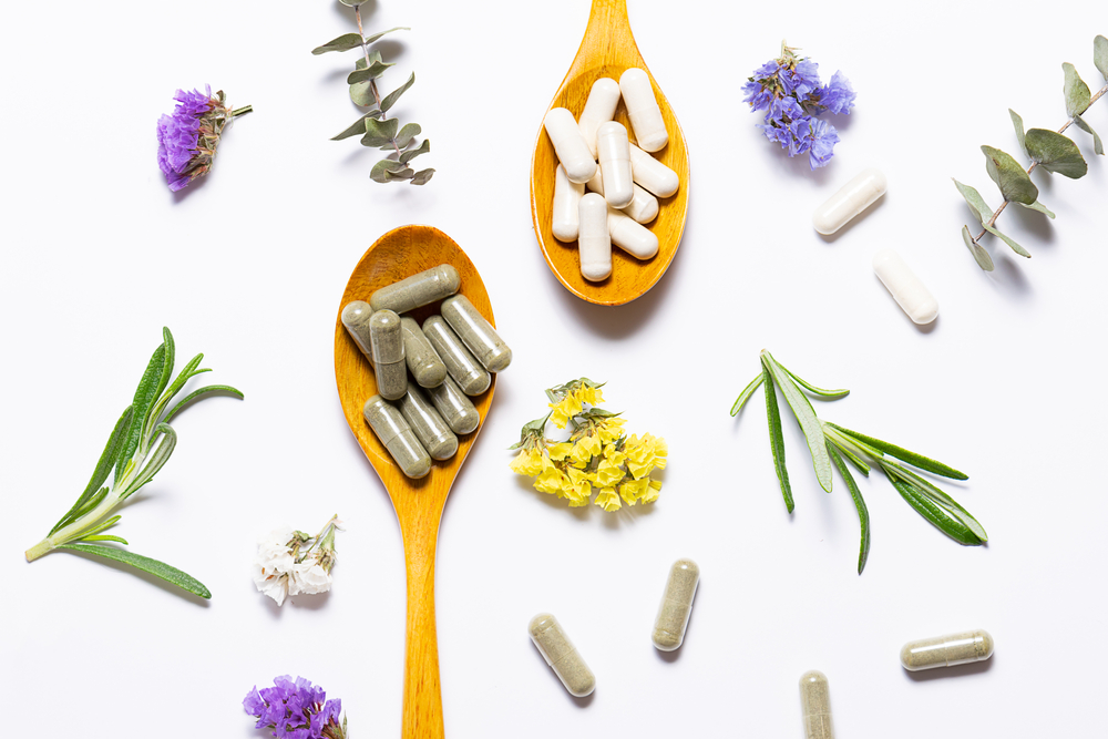 Capsules of natural collagen and herbal detox capsules for beauty and immunity support on white background with flowers and herbs top view. Healthy lifestyle concept.