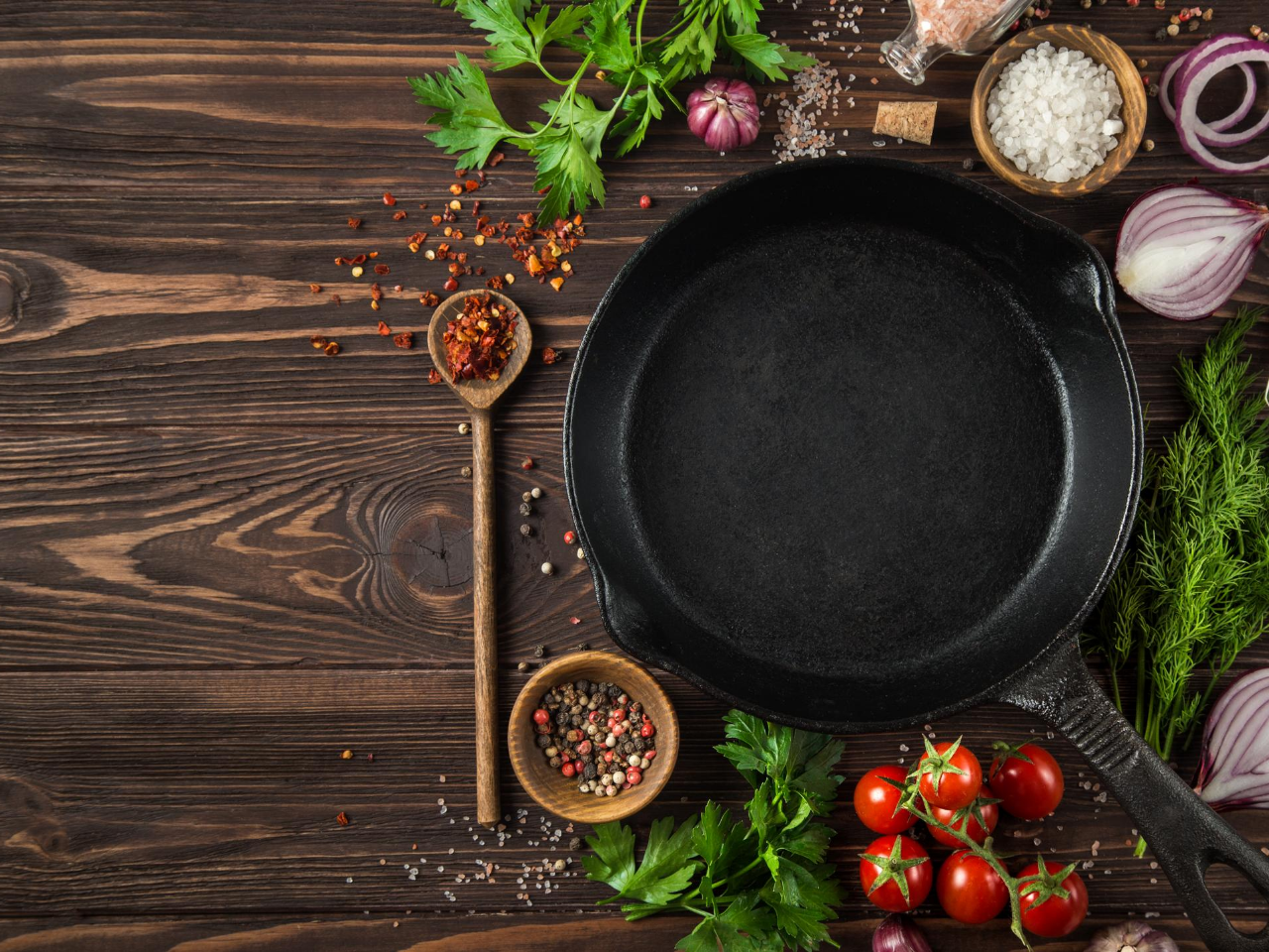 Cast iron pan on a wood table with spices and tomatoes