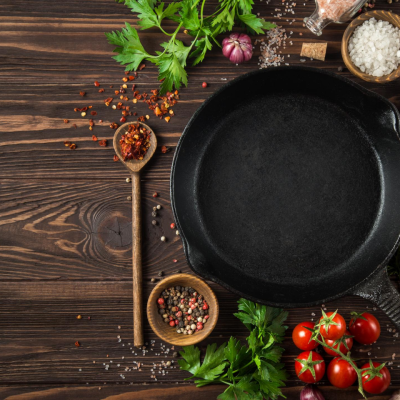 Cast iron pan on a wood table with spices and tomatoes