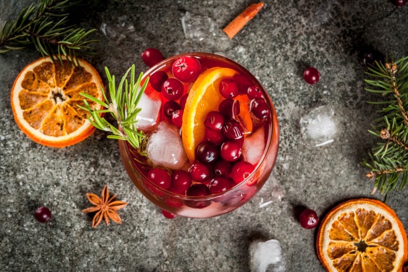 Christmas winter drinks. Cold cocktail with cranberries, orange, rosemary, with spices (cinnamon, anise) and ice, on a dark stone table, top view