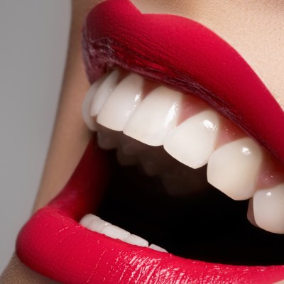 Close-up happy female smile with healthy white teeth, bright magenta lips make-up. Cosmetology, dentistry and beauty care. Macro of woman's smiling mouth