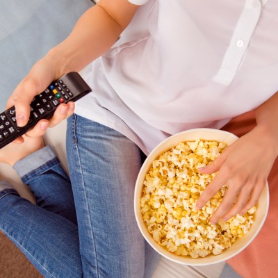 Close up of woman eating popcorn with remote control tv.