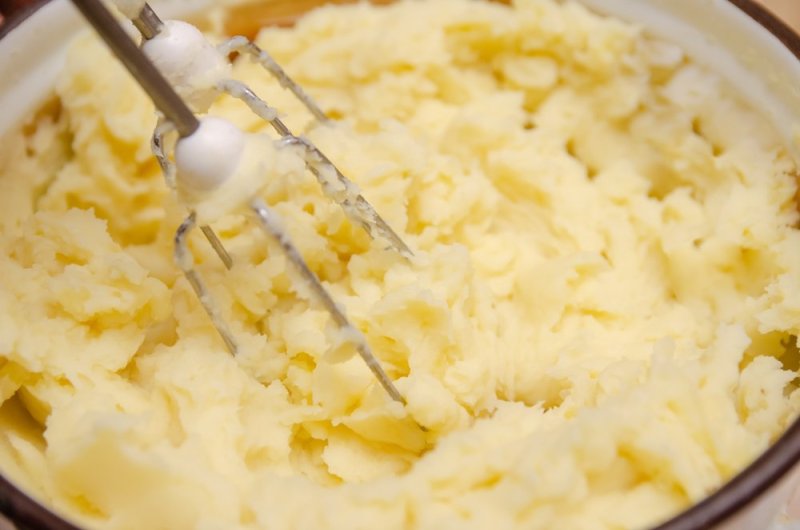 Close up woman's hand making mashed potato with mixer in saucepan. Cooking mashed potatoes.