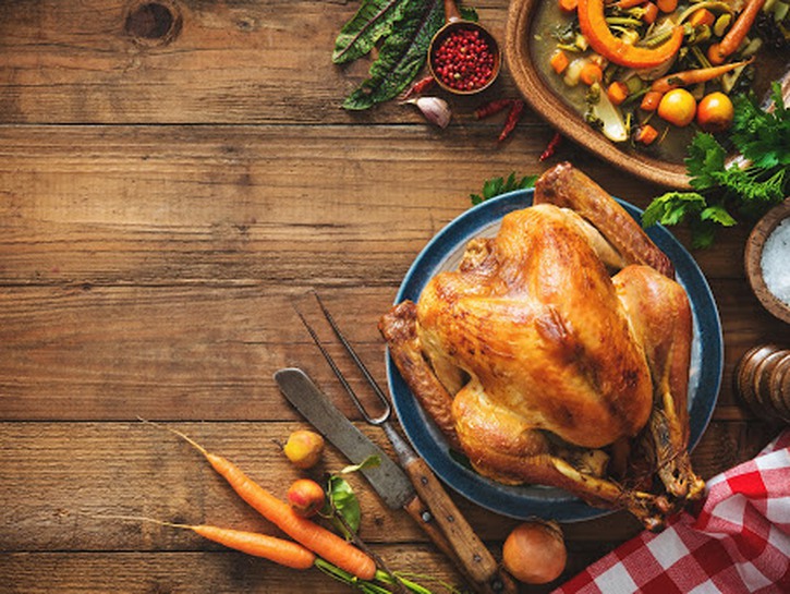 Cooked turkey on a wooden table with carrots carving knives and a checkered tablecloth