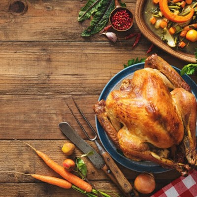 Cooked turkey on a wooden table with carrots carving knives and a checkered tablecloth