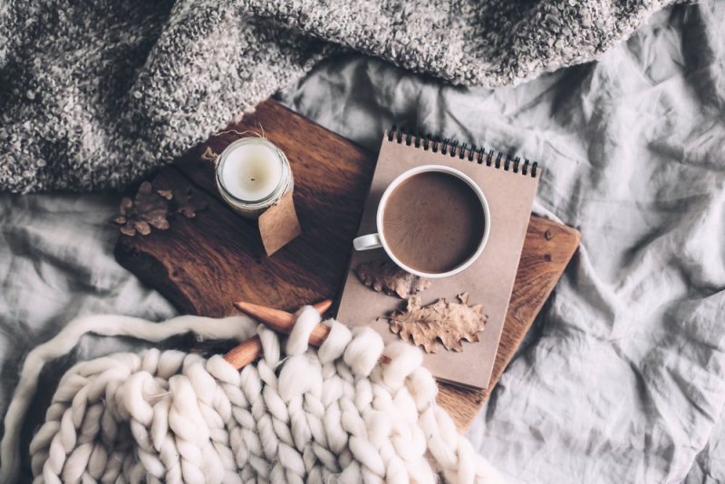 Cup of coffee and candle on rustic wooden serving tray in the cozy bed with blanket