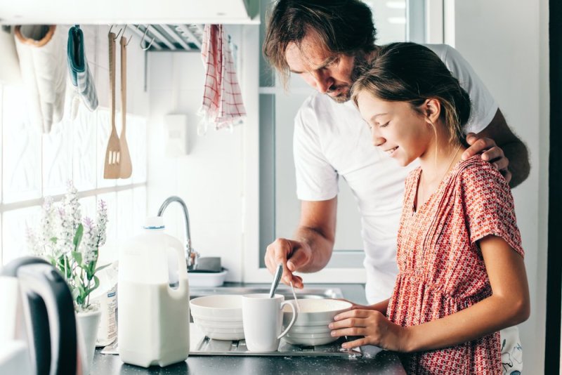 Dad with his 10 years old kid girl cooking in the kitchen, casual lifestyle photo series. Child making breakfast with parent together. Cozy homely scene.