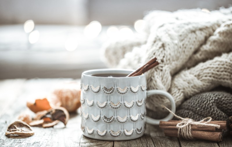 Details of still life in the home interior living room. Beautiful Cup of tea with tangerines and sweaters on wooden background . Cosy autumn-winter concept