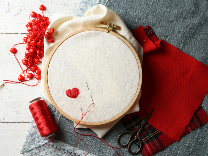 Embroidery hoop with small red heart on canvas, red thread, sewing supplies