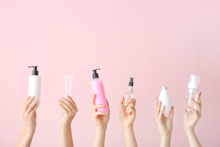 Female hands with different cosmetic products in bottles on color background
