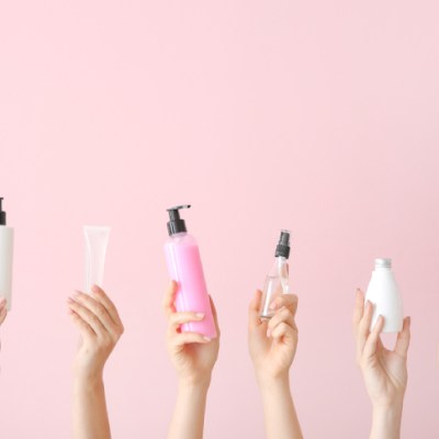 Female hands with different cosmetic products in bottles on color background