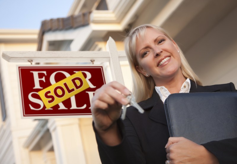 Female Real Estate Agent with Keys in Front of Sold Sign and Beautiful House.
