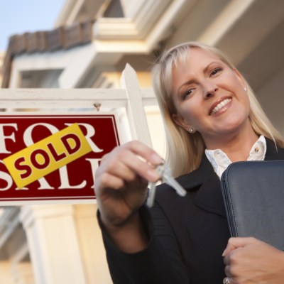 Female Real Estate Agent with Keys in Front of Sold Sign and Beautiful House.