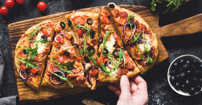 Flatbread pizza garnished with fresh arugula on wooden pizza board, top view