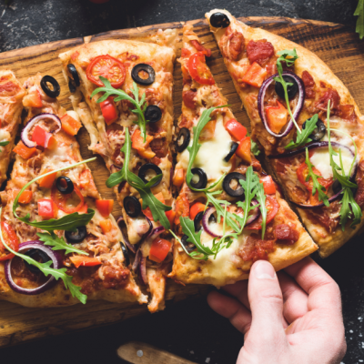 Flatbread pizza garnished with fresh arugula on wooden pizza board, top view