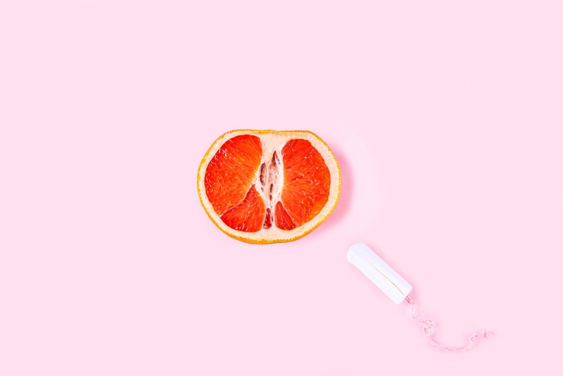 Fresh red cut grapefruit and tampon on pink background. Female health, Menstruation concept. Fruit as symbol of vagina. Close up