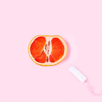 Fresh red cut grapefruit and tampon on pink background. Female health, Menstruation concept. Fruit as symbol of vagina. Close up
