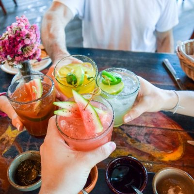 Friends toasting, saying cheers holding tropical blended fruit margaritas. Watermelon and passionfruit drinks.