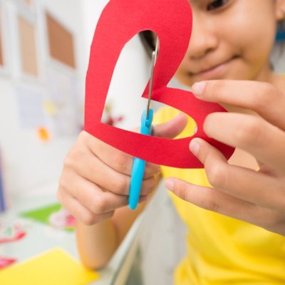 Girl cutting out paper heart, selective focus