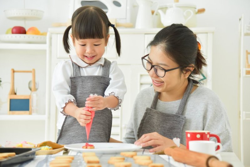 Happy Asian Kid and sister or young mother decorating cookies in the kitchen. Smiling family.