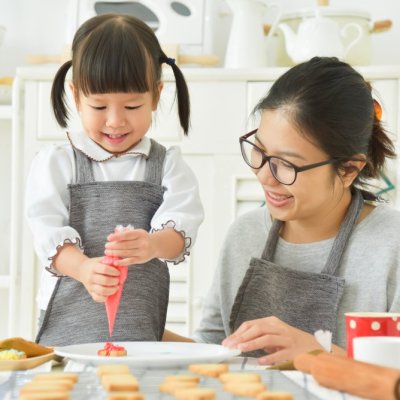 Happy Asian Kid and sister or young mother decorating cookies in the kitchen. Smiling family.
