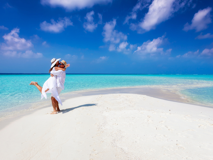 Happy couple in love is having fun and hugging on a sandbar with white sand and turquoise ocean