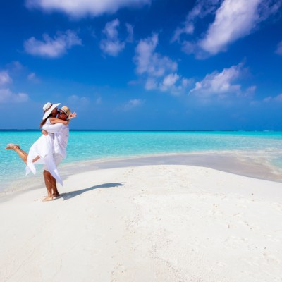 Happy couple in love is having fun and hugging on a sandbar with white sand and turquoise ocean