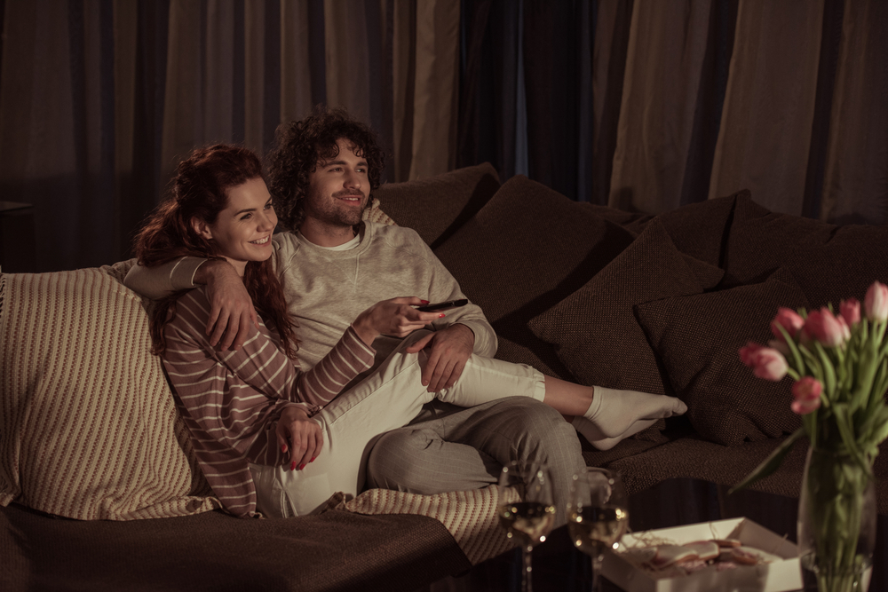 happy couple watching tv on sofa in evening