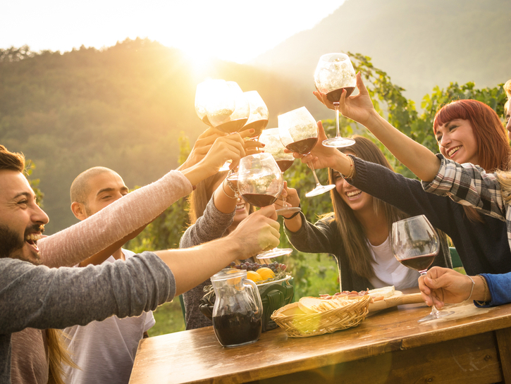 Happy friends having fun outdoor - Young people enjoying harvest time together outside at farm house vineyard countryside - Youth friendship concept - Hands toasting red wine glass at winery on sunset