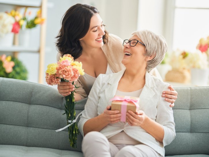 Happy mother's day! Beautiful young woman and her mother with flowers and gift box at home