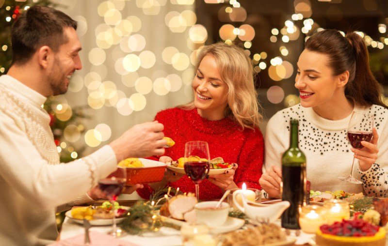 holidays and celebration concept - happy friends having Christmas dinner at home, eating, and drinking