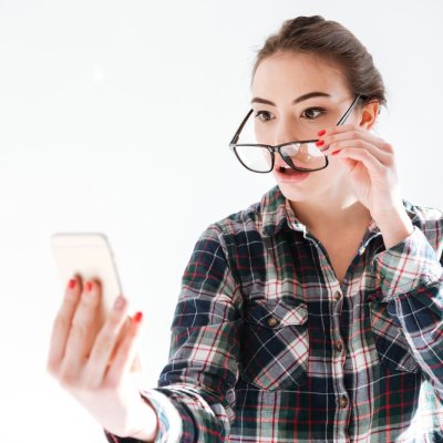 Image of confused woman wearing glasses standing over white background while look at phone