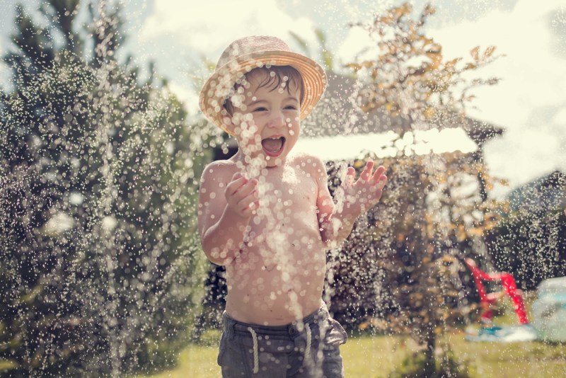 Little boy in sun hat playing in the sprinklers