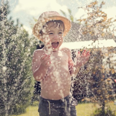 Little boy in sun hat playing in the sprinklers