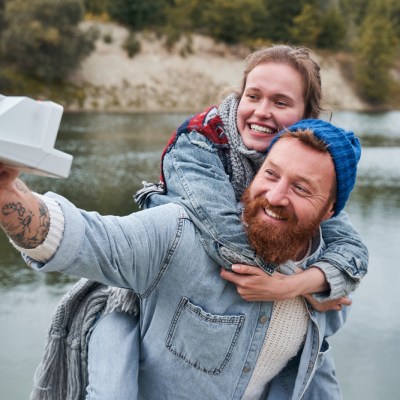 Love and date concept. Young happy caucasian woman brightly smiling while her beloved male carefully holding her on his back. Couple taking selfie with a Polaroid